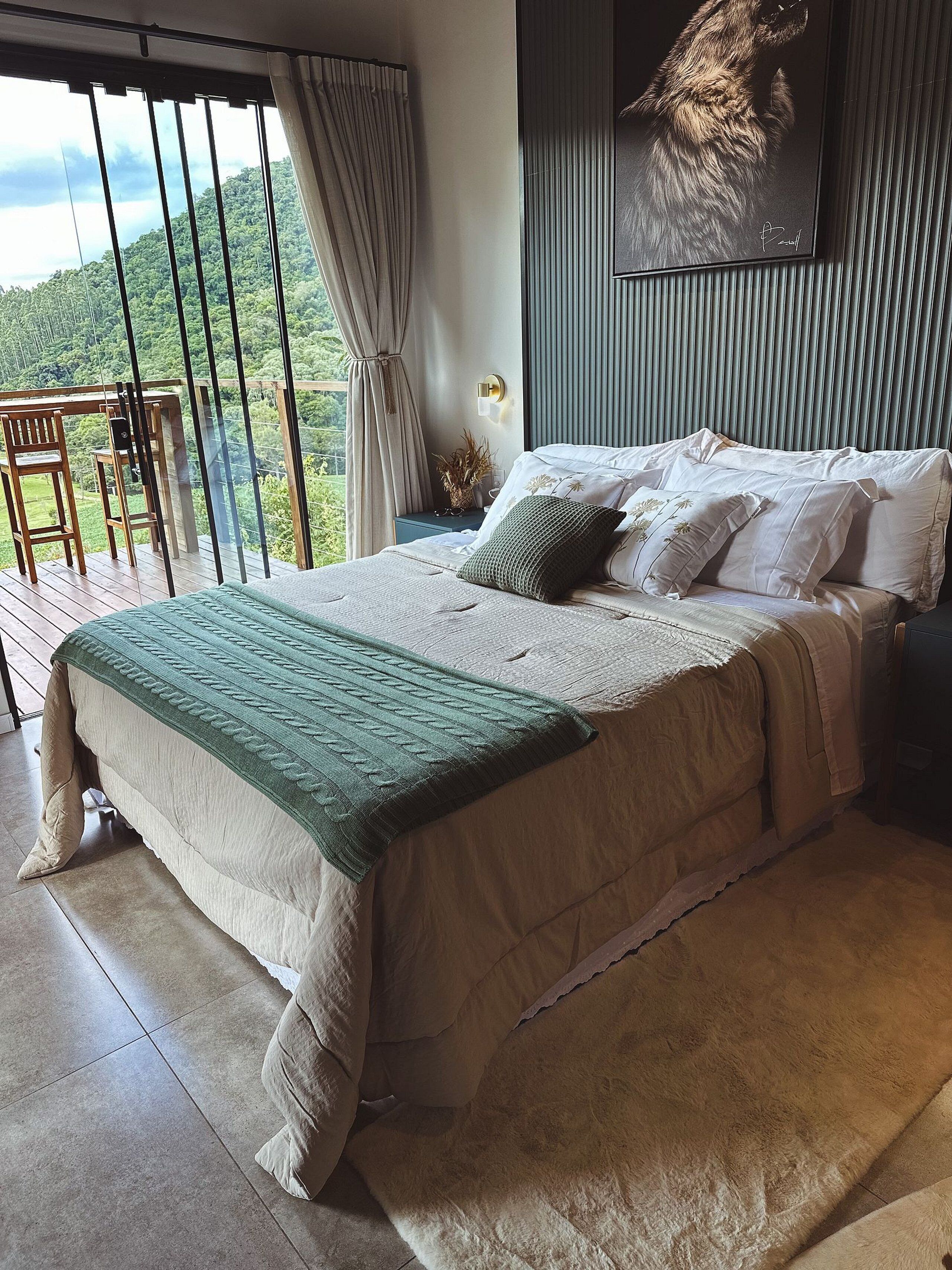 A bedroom with a large bed, a view of a balcony, and a painting on the wall.
