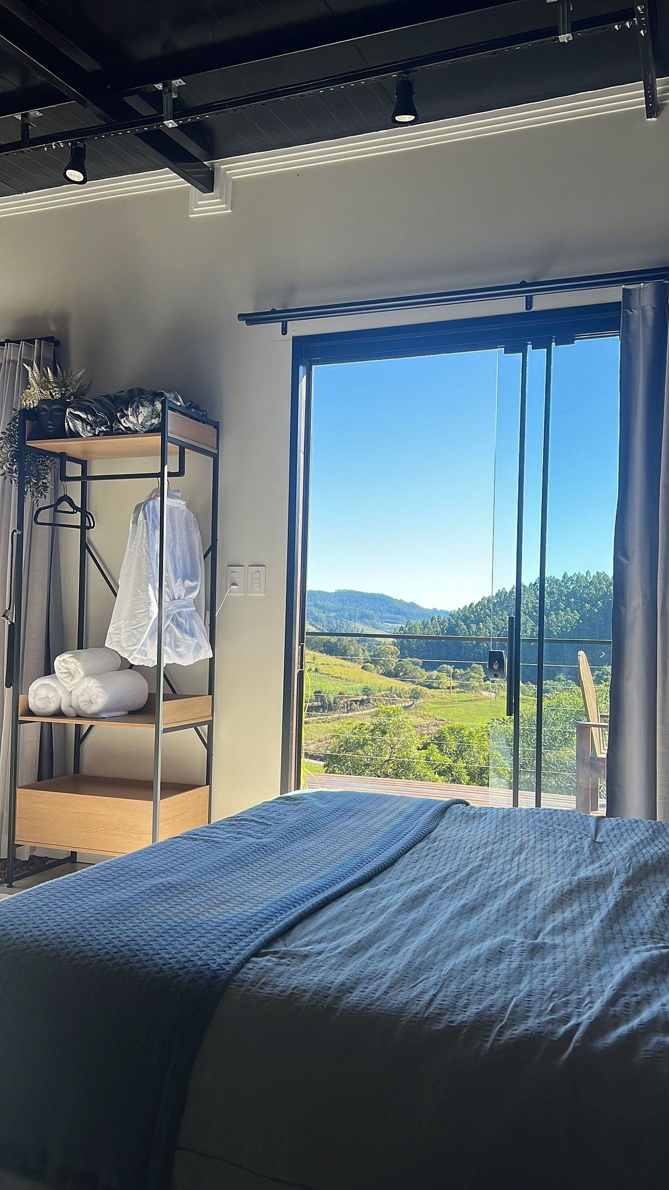 Un dormitorio con una cama, un armario y vistas a un paisaje a través de un ventanal grande.