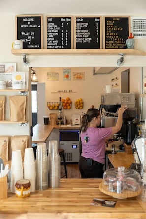 A coffee shop interior with a menu board, coffee machines, and a counter with disposable cups. - 4BR Sebastian Getaway • Beaches, Surf & Fishing (Sebastian)