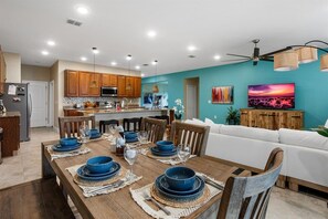 Una cocina moderna con armarios de madera, un comedor con vajilla azul y una sala de estar con sofá blanco y paredes verde azulado.