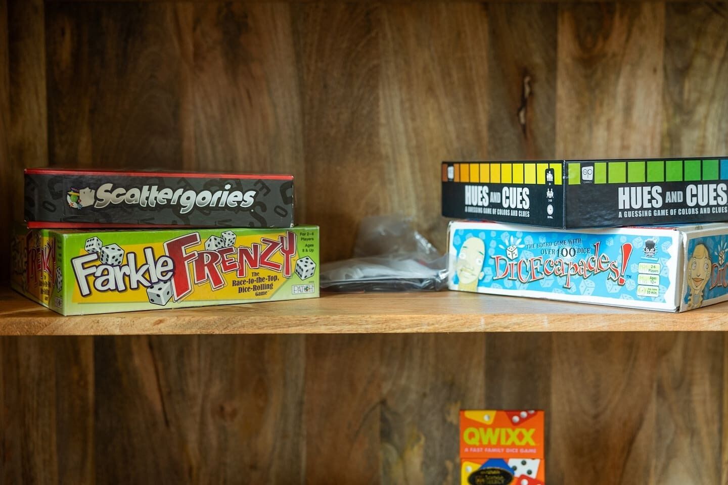 Una estantería con varios juegos de mesa, incluyendo 'Scattergories', 'Farkle Frenzy', 'Hues and Cues', 'Dicecapades' y 'QWIXX'.