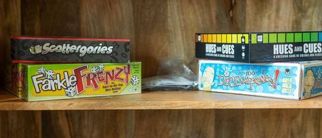 Una estantería con varios juegos de mesa, incluyendo 'Scattergories', 'Farkle Frenzy', 'Hues and Cues', 'Dicecapades' y 'QWIXX'.