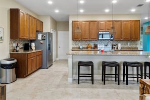 Una cocina moderna con armarios de madera, encimeras de granito, electrodomésticos de acero inoxidable e iluminación colgante.