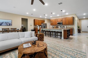 A modern living room with a sofa, wooden coffee table, and a kitchen area with wooden cabinets and a bar. - 4BR Sebastian Getaway • Beaches, Surf & Fishing (Sebastian)