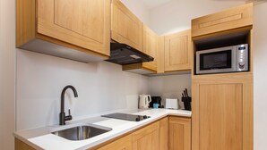 A modern kitchen with wooden cabinets, a stainless steel sink, a black range hood, a microwave, and a kettle. - Comfortable Apartment - 1br/2p - Le Marais (Paris)