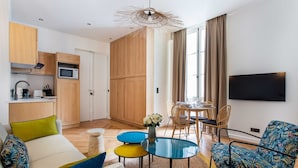 A modern living room with a sofa, a dining table, and chairs. There is a kitchen area with a microwave and cabinets. A flat-screen TV is mounted on the wall. - Comfortable Apartment - 1br/2p - Le Marais (Paris)
