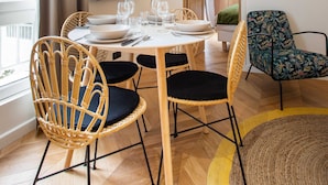 A dining area with a round table set for four, surrounded by wicker chairs with black cushions. A flat-screen TV is mounted on the wall above the table. - Comfortable Apartment - 1br/2p - Le Marais (Paris)
