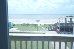 A beach view from a balcony with a wooden deck, a pathway leading to the beach, and a building with a sign that reads 'BOLIBAR'.