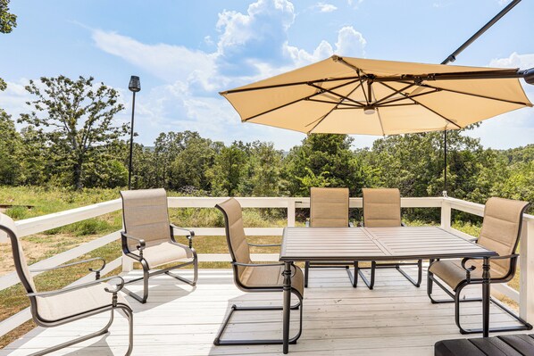 A deck with a table and chairs, surrounded by a white railing, overlooking a natural landscape.