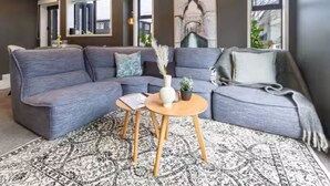 A modern living room with a grey sectional sofa, a small round wooden coffee table, and a patterned rug.