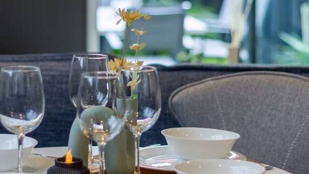 A dining table set with white plates, bowls, and wine glasses, accompanied by a candle and a vase with flowers.