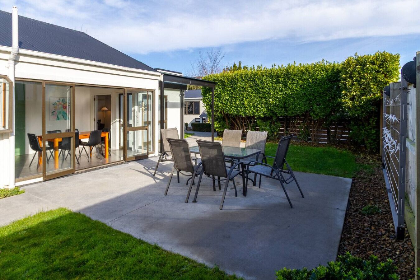 A patio with a glass table and chairs, a covered seating area, and a well-maintained lawn.