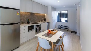 Eine moderne Küche mit einem Edelstahl-Kühlschrank, einem Backofen und einer Spüle. Ein Esstisch mit Stühlen und eine Blumenvase stehen bereit.