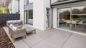 A modern outdoor patio with wicker furniture, a glass door leading to a dining area, and a view of the surrounding buildings.