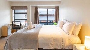 A hotel room with a bed, a desk, a chair, and a window with curtains.