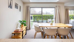 A modern dining area with a large table, chairs, and a view of a garden through large windows.