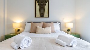 A neatly made bed with white linens, two pillows, and rolled towels on a green nightstand. - Urban Utopia 2 Bedroom Retreat (Christchurch)