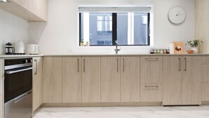 A modern kitchen with light wood cabinets, a built-in oven, and a window with a view of the outside. - Urban Utopia 2 Bedroom Retreat (Christchurch)