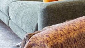 Un sofá gris con un plaid blanco y dos cojines naranja.