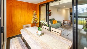 Un comedor con una mesa de madera y bancos, una planta en maceta y vistas a una sala de estar con un sofá y una mesa baja.