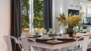 A dining area with a table set for four, white chairs, and a vase with green leaves.