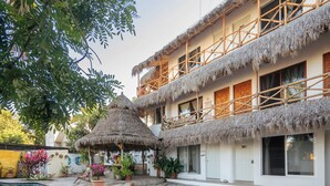 A building with a pool, thatched-roof structures, and potted plants.