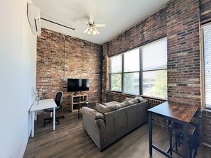 A living room with a brick wall, a flat-screen TV, a sofa, a dining table, and a ceiling fan.