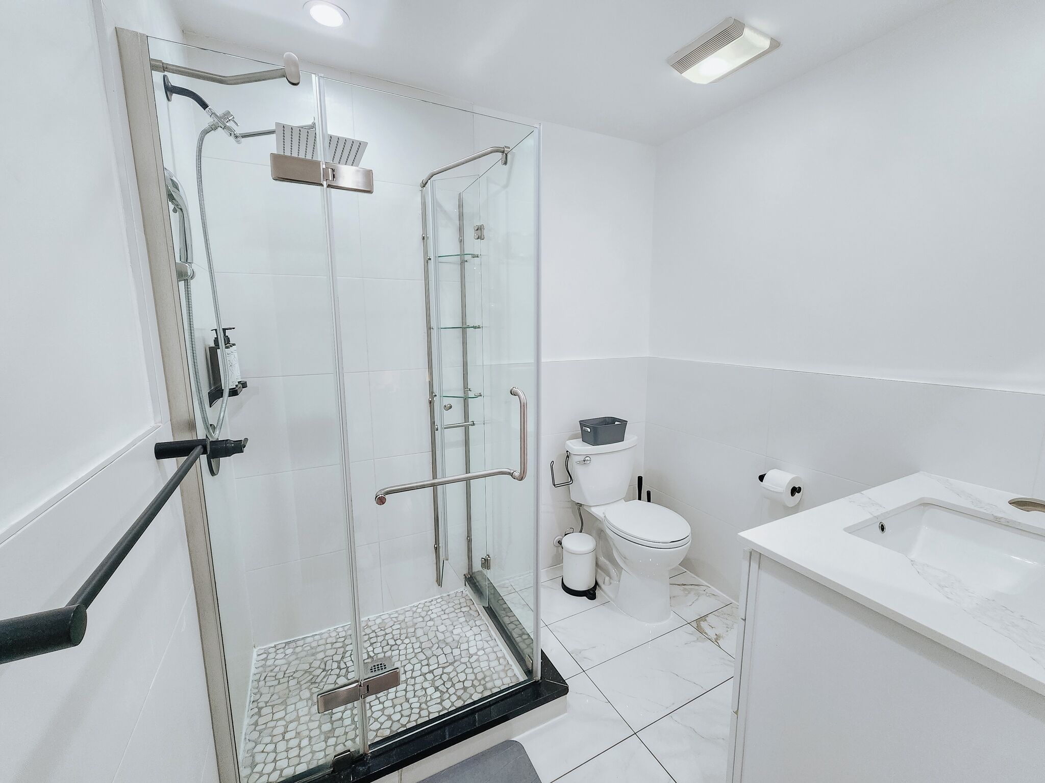 A modern bathroom with a glass-enclosed shower, a white toilet, and a marble sink.