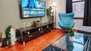 Una sala moderna con un televisor de pantalla plana montado en la pared, un sillón azul, una mesa de centro de vidrio y un mueble de entretenimiento de madera.