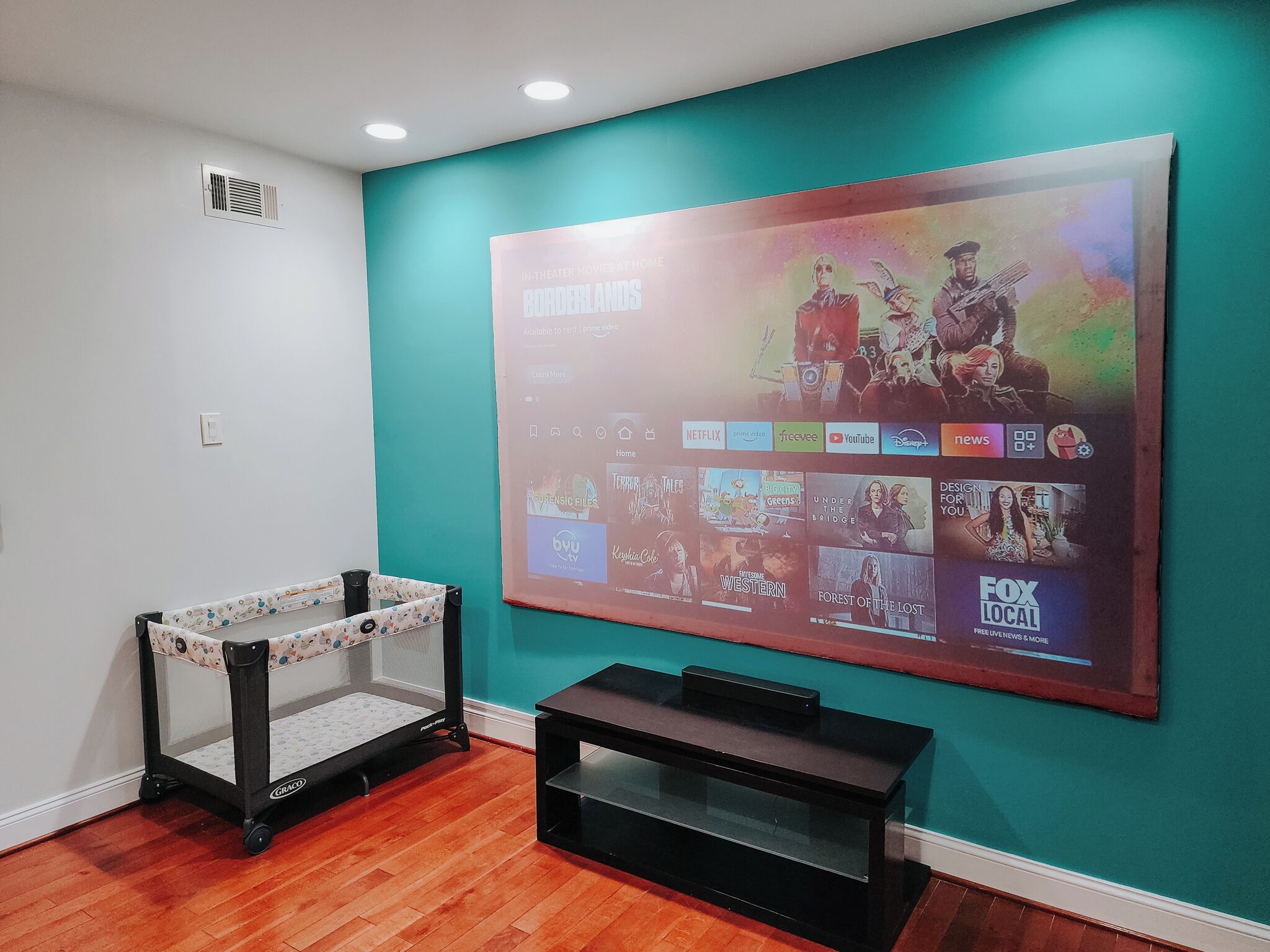 A room with a teal accent wall, a mounted TV displaying movie options, a baby stroller, and a black entertainment unit.