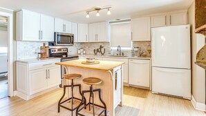 Une cuisine moderne avec des meubles blancs, un îlot central en bois doté de tabourets, des appareils électroménagers en acier inoxydable et un réfrigérateur blanc.