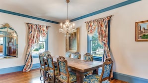 A dining room with a wooden table and chairs, blue patterned curtains, and a chandelier.
