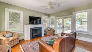 A living room with a fireplace, leather sofa, armchair, and a flat-screen TV mounted above the fireplace.