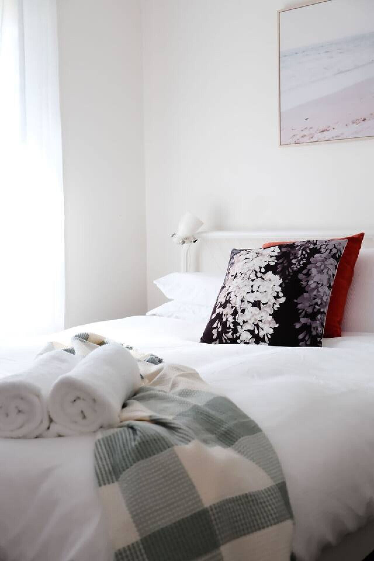 A neatly made bed with white linens, a floral pillow, and a plaid blanket.