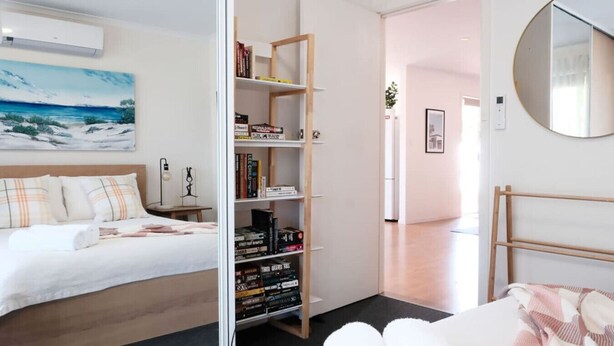 Una habitación de hotel moderna con una cama, una estantería, un escritorio y un espejo grande.
