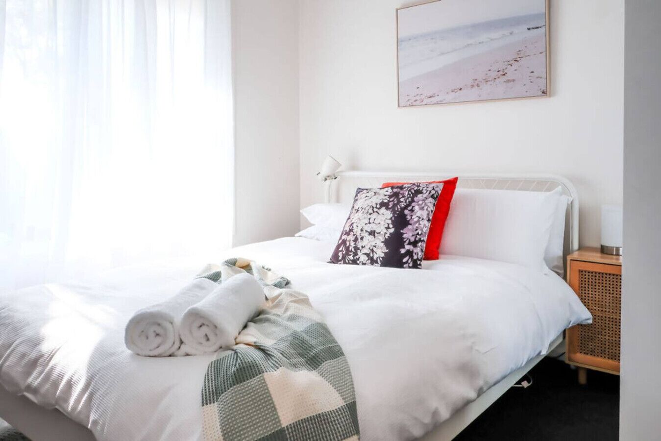 A neatly made bed with rolled towels, a floral pillow, and a checkered blanket.