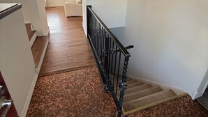 A staircase with a black railing leading to a landing. The landing has a chandelier and a view of a balcony with a white couch. - Spacious 3-bedroom Lakeview Home Centrally Located in Quiet Neighborhood (Moses Lake)