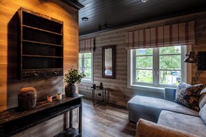 A cozy room with a wooden wall, a sofa, a small table with a plant, and a window with a view of greenery. - Bokhandel'n Gjestehus (Vaga)