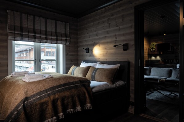 A cozy bedroom with a bed, a window with blinds, a wall-mounted light, and a view of the outside. - Bokhandel'n Gjestehus (Vaga)