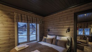 Una camera da letto accogliente in legno con un letto grande, una finestra con persiane e vista su un paesaggio innevato.