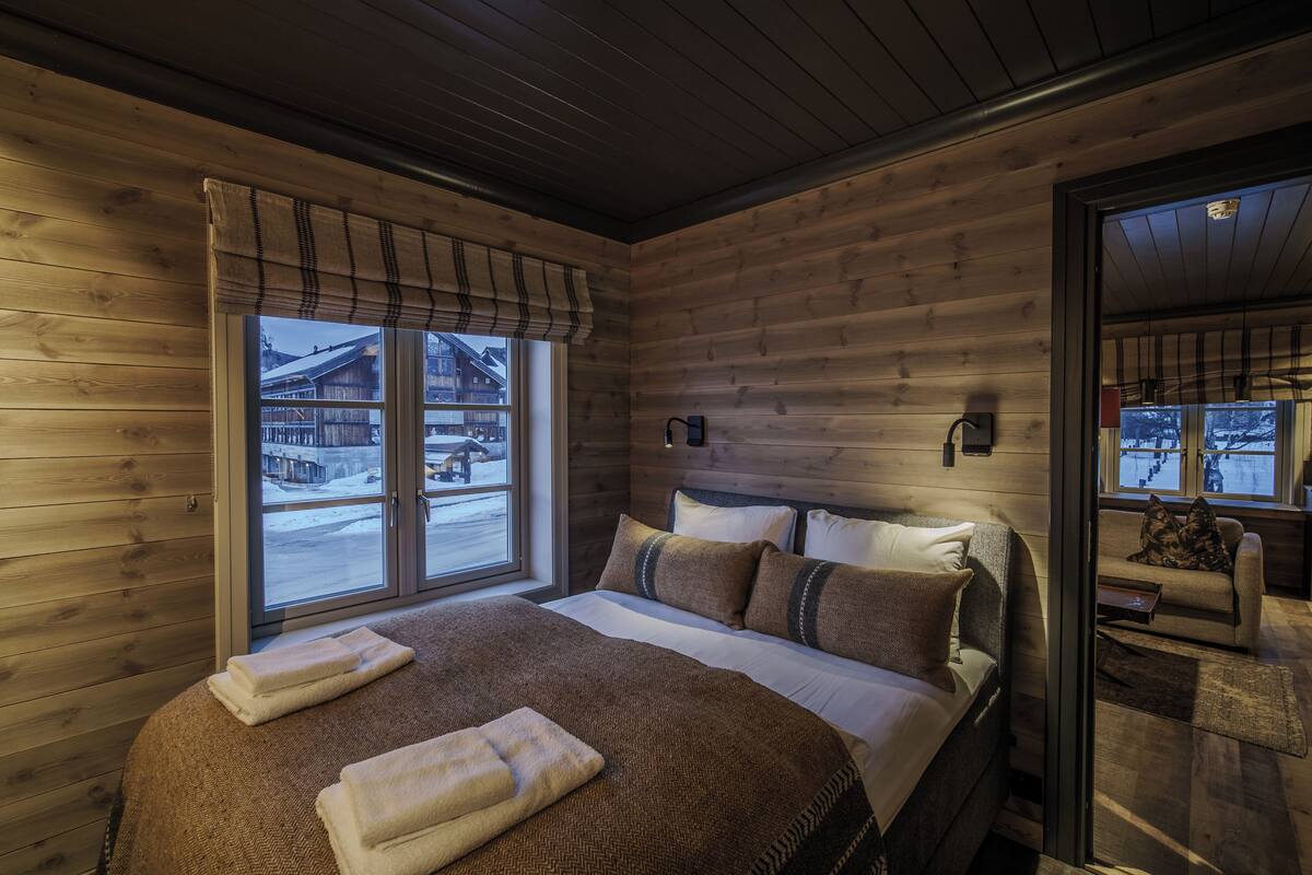 Une chambre confortable dans un chalet en bois, avec un grand lit, une fenêtre équipée de stores et une vue sur un paysage enneigé.