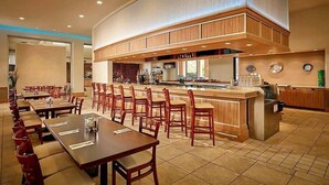 Un ristorante con lunghi tavoli comuni, una zona bar e una cucina sullo sfondo.