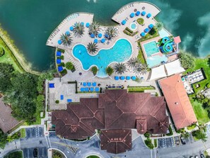 Vista aérea de un complejo turístico con una gran piscina central, piscinas más pequeñas y un tobogán de agua.