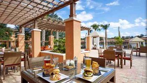 Un'area pranzo all'aperto con tavoli e sedie, coperta da una pergola e circondata da palme.