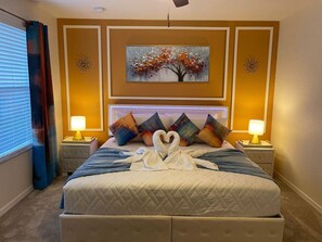 Una habitación de hotel con una cama grande, dos mesitas de noche con lámparas, un cuadro de un árbol y una decoración de toallas en forma de corazón.
