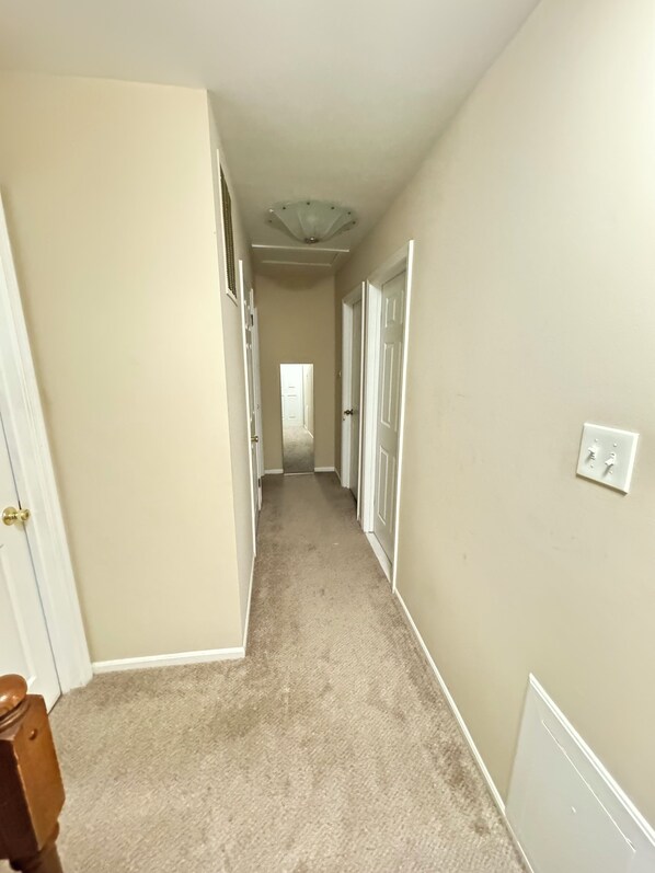 A hallway with beige walls, white doors, and a carpeted floor.