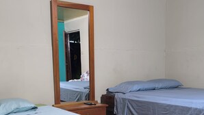 A room with two beds, a wooden dresser, and a large mirror.