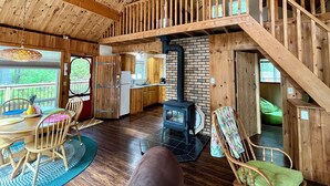 A rustic cabin interior with a wooden staircase, a kitchen area, and a seating area with a fireplace.