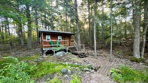 A cabin with a wooden deck, surrounded by dense forest.