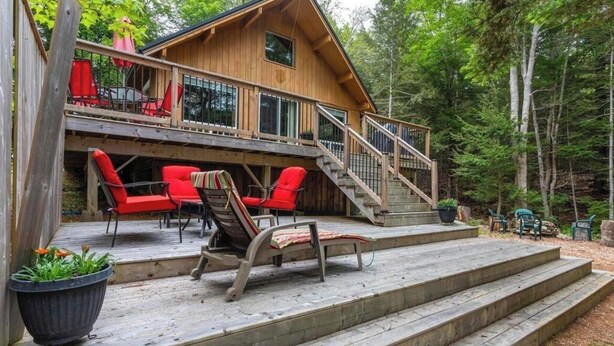 A wooden cabin with a deck, outdoor seating, and a staircase leading to the upper level.